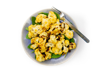 overhead view of oven baked curried cauliflower on a blue plate isolated on white