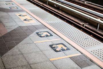 Fototapeta premium Arrow symbol or sign on platform in the queue waiting for the sky train. Yellow arrows on floor platform at sky-train station. Sign for passenger train that is ridden primarily by commuters.