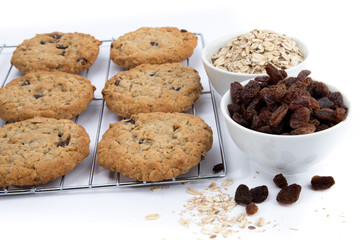 oatmeal raisin cookies on a wire cooling rack with a cup of raisins and a cup of oatmeal isolated on white
