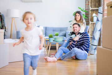 Beautiful family sitting on the floor playing with his kid at new home around cardboard boxes