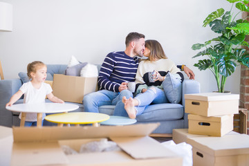 Beautiful family, parents sitting on the sofa drinking coffee looking his kid playing at new home around cardboard boxes