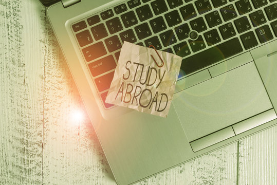 Text sign showing Study Abroad. Business photo text live in a foreign country and attend a foreign university Trendy metallic laptop crushed colored paper note lying old wooden table