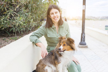 Young beautiful woman sitting on bench in the prominade with her dog