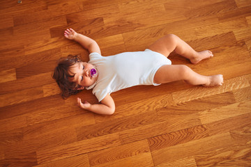 Beautiful toddler child girl wearing white bodysuit lying down on the floor using pacifier