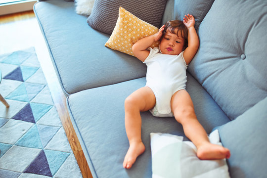 Beautiful toddler child girl wearing white bodysuit lying down on the sofa