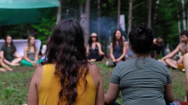 Diverse people enjoy spiritual gathering Two women are viewed from behind sitting in a circle with a mixed group of people, listening to a shaman teacher during a weekend of multicultural experiences.