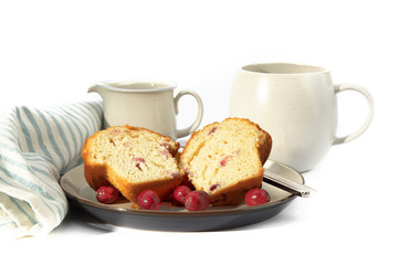 a cranberry lemon muffin cut in half on a plate with a coffee cup with a green napkin isolated on white