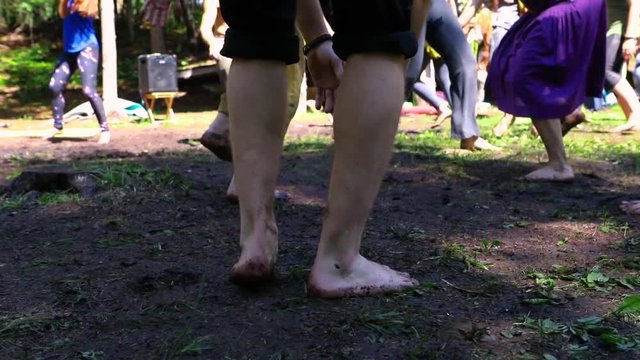 Diverse people enjoy spiritual gathering A closeup view on the naked legs and feet of a caucasian male during a playful and free dance routine at a sacred woodland retreat seeking enlightenment.