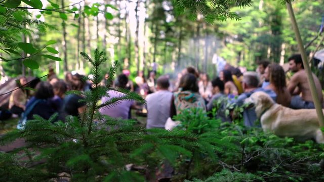 Diverse people enjoy spiritual gathering Slowed down footage of an intergenerational group of people sitting together during a woodland retreat, blurred in the background with golden retriever dog.