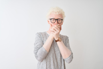 Young albino blond man wearing striped t-shirt and glasses over isolated white background shocked covering mouth with hands for mistake. Secret concept.
