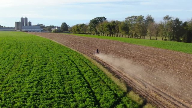 Aerial tracking shot of 4-wheeler, ATV speeding through farm field, dust cloud behind