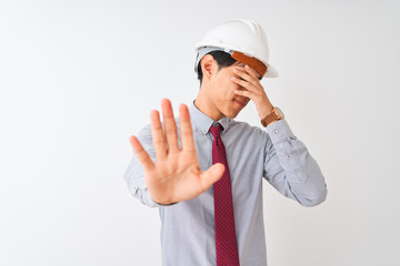 Chinese architect man wearing tie and helmet standing over isolated white background covering eyes with hands and doing stop gesture with sad and fear expression. Embarrassed and negative concept.