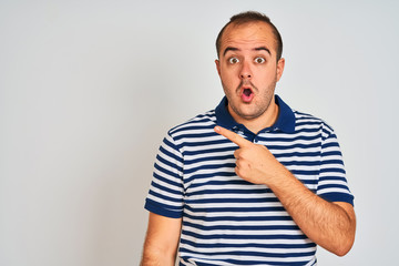 Young man wearing casual striped polo standing over isolated white background Surprised pointing with finger to the side, open mouth amazed expression.