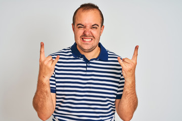 Fototapeta premium Young man wearing casual striped polo standing over isolated white background shouting with crazy expression doing rock symbol with hands up. Music star. Heavy music concept.