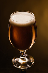 close up view of beer with foam in glass on dark background with lighting