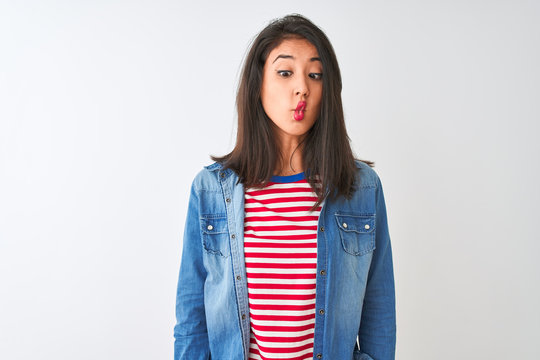 Young chinese woman wearing striped t-shirt and denim shirt over isolated white background making fish face with lips, crazy and comical gesture. Funny expression.