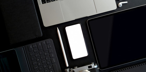 Top view of dark trendy workspace with blank screen smartphone and other electronics with office...