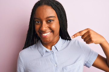 Fototapeta na wymiar Young african american woman wearing striped shirt standing over isolated pink background with surprise face pointing finger to himself