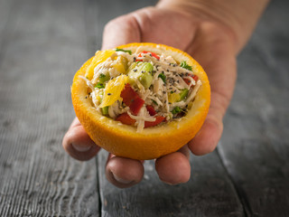 Half an orange with chicken salad and avocado in the man's hand.