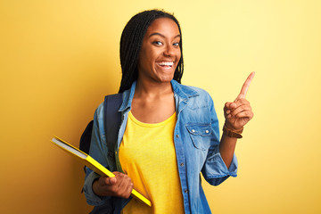 African american student woman wearing backpack and book over isolated yellow background very happy pointing with hand and finger to the side