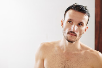 Obraz premium Handsome young man with beautiful skin looking at mirror after taking shower in bathroom