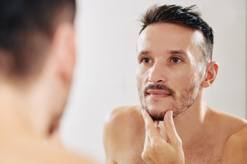 Young man touching his chin and checking his beard he is trying to grow out