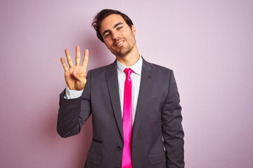 Young handsome businessman wearing suit and tie standing over isolated pink background showing and pointing up with fingers number four while smiling confident and happy.