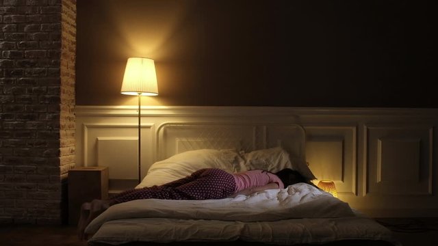 a young beautiful girl in pink pajamas comes late at night to the bed with white linens and collapses onto the blanket. A tired woman falls asleep after a hard day.