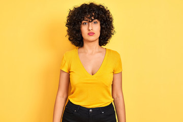 Young arab woman with curly hair wearing t-shirt standing over isolated yellow background Relaxed with serious expression on face. Simple and natural looking at the camera.