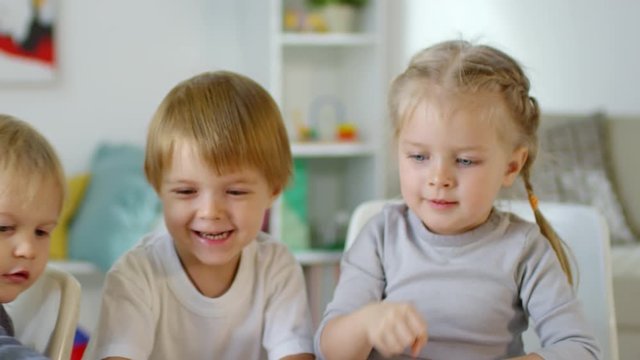 Happy little boys and girl slapping toy tower and smiling as it crushing down on table while playing together in kindergarten