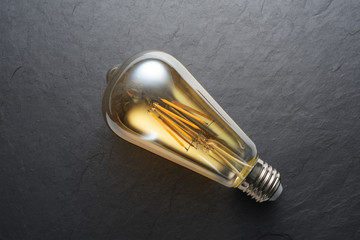 Transparent LED filament light bulb on black slate background.