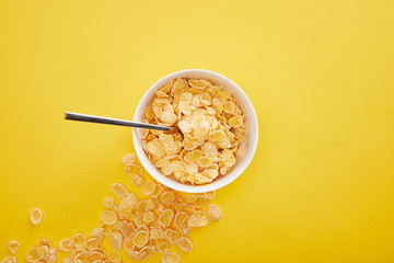 top view of bowl with cornflakes near scattered pieces isolated on yellow