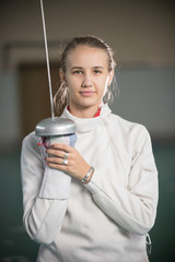 A young smiling woman fencer standing in the gym with a sword up