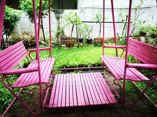 Pink old swings in a playground on green grass among the trees