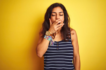 Young beautiful woman wearing striped t-shirt standing over isolated yellow background bored yawning tired covering mouth with hand. Restless and sleepiness.