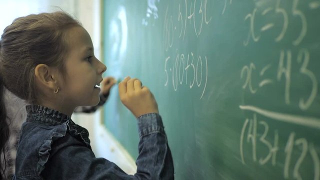 Elementary school. Little schoolgirl writing numbers on green chalk board in classroom
