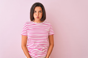Young beautiful woman wearing striped t-shirt standing over isolated pink background puffing cheeks with funny face. Mouth inflated with air, crazy expression.