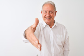 Senior grey-haired man wearing elegant shirt standing over isolated white background smiling friendly offering handshake as greeting and welcoming. Successful business.