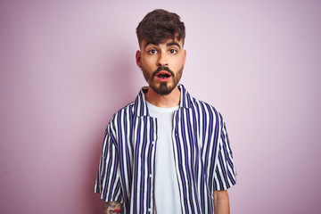 Young man with tattoo wearing striped shirt standing over isolated pink background afraid and shocked with surprise expression, fear and excited face.