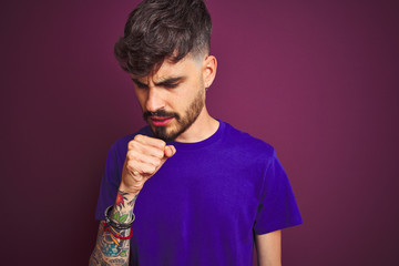 Young man with tattoo wearing t-shirt standing over isolated purple background feeling unwell and coughing as symptom for cold or bronchitis. Healthcare concept.
