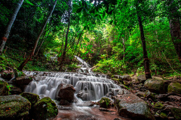 Natural blurred background of waterfalls, fast-flowing currents and water droplets from the wind blowing among the rocks and surrounded by big trees, spontaneous beauty
