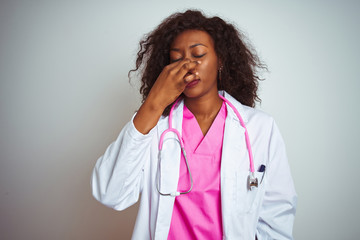 African american doctor woman wearing  pink stethoscope over isolated white background smelling something stinky and disgusting, intolerable smell, holding breath with fingers on nose.