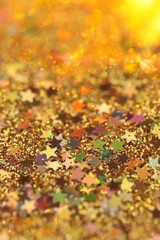 Christmas and New Year background. Stars and golden glitter on a blurry gold background.Golden shiny macro texture.