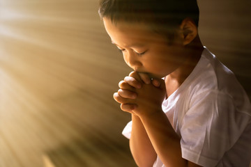 boy praying to God with hands held together with closed eyes