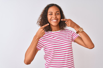 Young brazilian woman wearing pink striped t-shirt standing over isolated white background smiling cheerful showing and pointing with fingers teeth and mouth. Dental health concept.