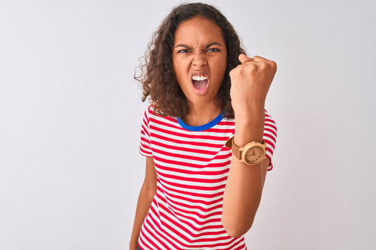 Young brazilian woman wearing red striped t-shirt standing over isolated white background angry and mad raising fist frustrated and furious while shouting with anger. Rage and aggressive concept.