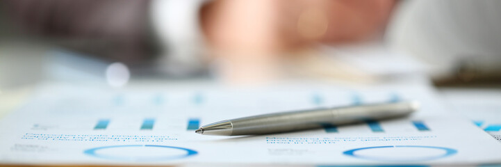 Silver pen lie at important paper on table in office closeup with businessman in background. Paperwork job trade balance bank credit loan money invest payment irs commerce partnership concept - obrazy, fototapety, plakaty