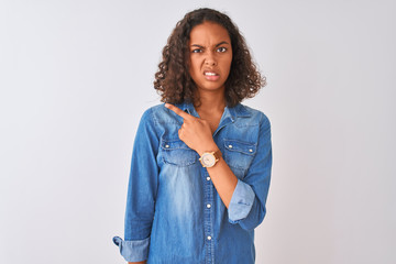 Young brazilian woman wearing denim shirt standing over isolated white background Pointing aside...