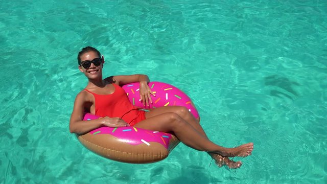 Beach summer vacation happy holiday girl floating relaxing on inflatable fun donut pool float in ocean turquoise Caribbean water swimming in tropical travel destination.