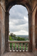 Medieval architecture. Large arch in the wall with a banister and with a beautiful Italian landscape. Focus on background